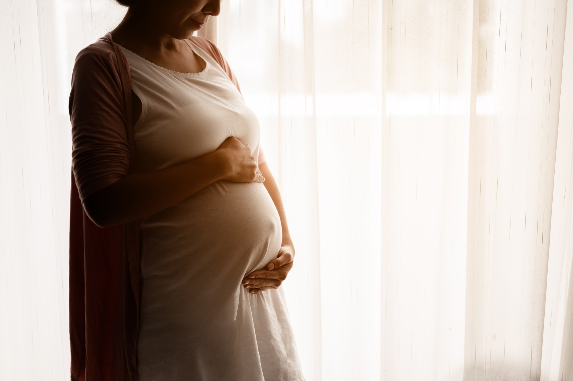 Schwangere Frau am Fenster hält ihren Bauch